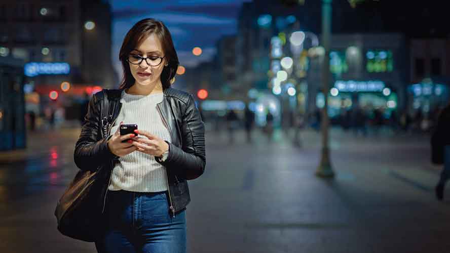 woman walking at night looking at her smart phone