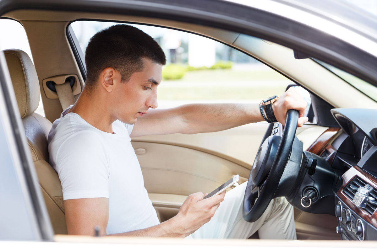 male sitting in car driver seat looking at his cellphone